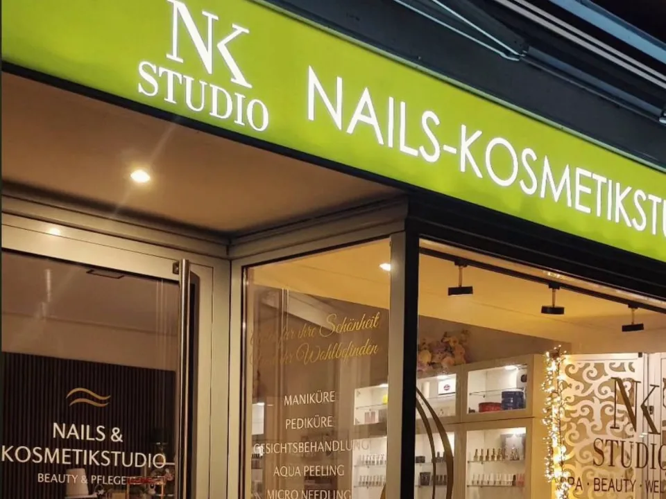Beleuchtetes Fassadenschild und beschriftete Schaufenster eines Kosmetikstudios am Abend
