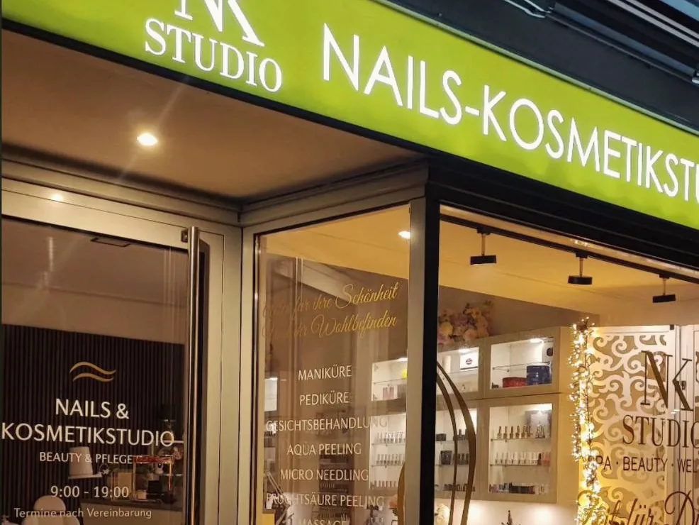Beleuchtetes Fassadenschild und beschriftete Schaufenster am Abend